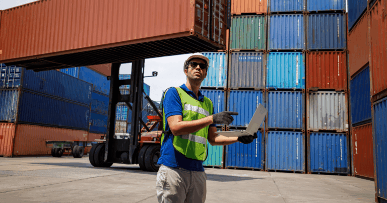 Profissional de logística em terminal portuário com laptop, inspecionando containers e representando a aplicação dos incoterms na operação de comércio exterior.