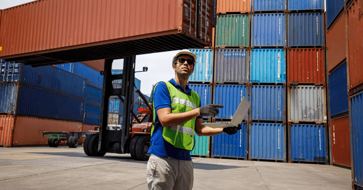 Profissional de logística em terminal portuário com laptop, inspecionando containers e representando a aplicação dos incoterms na operação de comércio exterior.
