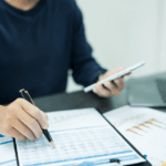 Profissional analisando relatórios financeiros e gráficos com foco em legislação tributária empresarial, ao lado de notebook e calculadora.