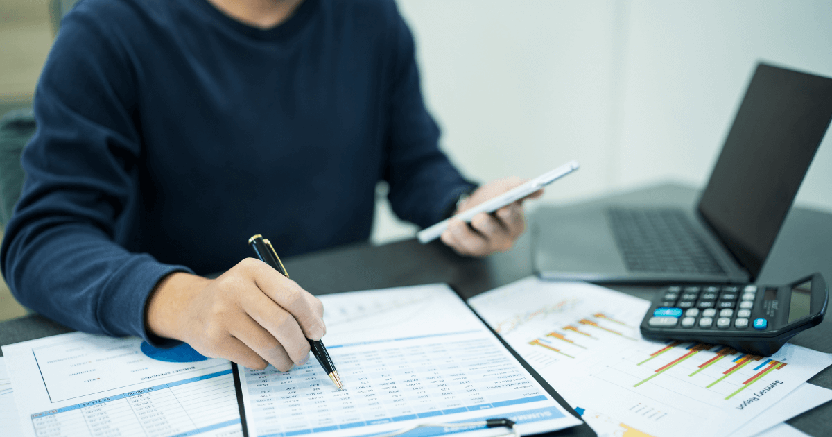 Profissional analisando relatórios financeiros e gráficos com foco em legislação tributária empresarial, ao lado de notebook e calculadora.