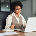 Profissional sorrindo durante reunião one a one online, com notebook, anotações e fone de ouvido, representando a prática de 1:1 nas empresas.
